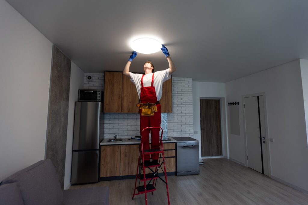 Electrician at work. Service for the repair of electrical wiring and replacement of ceiling lamps. A builder is installing a loft-style wooden ceiling. Rent-a-gent helps with the housework